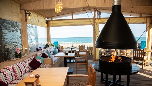 Un espace extérieur aménagé avec des sièges, offrant une vue sur l’océan, du mobilier en bois et un grand barbecue noir.
