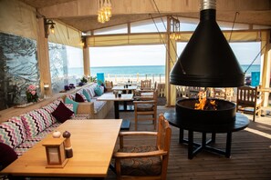 An outdoor seating area with a view of the ocean, wooden furniture, and a large black grill.