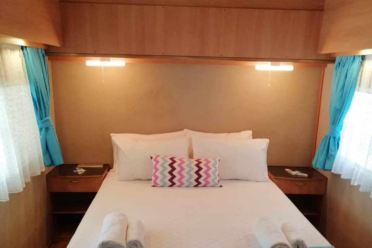 Ein ordentlich bezogenes Bett mit weißen Leinen und einer türkisfarbenen Tagesdecke, begleitet von zwei Nachttischen mit Lampen, in einem Zimmer mit Holzvertäfelung und Vorhängen.