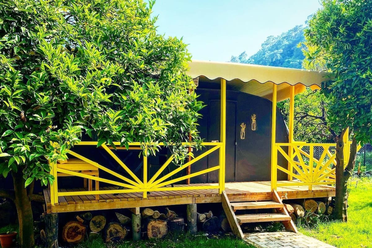 Eine Holzhütte mit gelben Geländern, einer überdachten Veranda und einer Treppe, die hinaufführt.