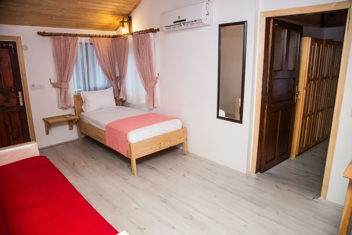 Ein Schlafzimmer mit einem hölzernen Bett, einem Nachttisch, einer roten Decke, einem Holzschrank und einem Spiegel an der Wand.
