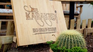 Une enseigne en bois portant l’inscription « KARAKEDY BEACH-BUNGALOW RESTAURANT » et un cactus au premier plan.