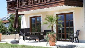 Een terras met tuinmeubilair, een potpalmhout en een balkon met houten hekwerk.