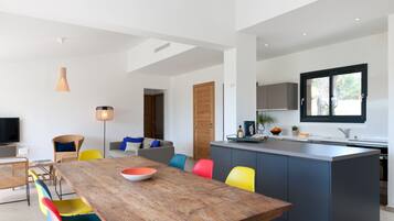 Une cuisine moderne dotée d’un îlot central, d’un coin repas avec des chaises aux couleurs vives et d’une grande fenêtre qui laisse entrer la lumière naturelle.