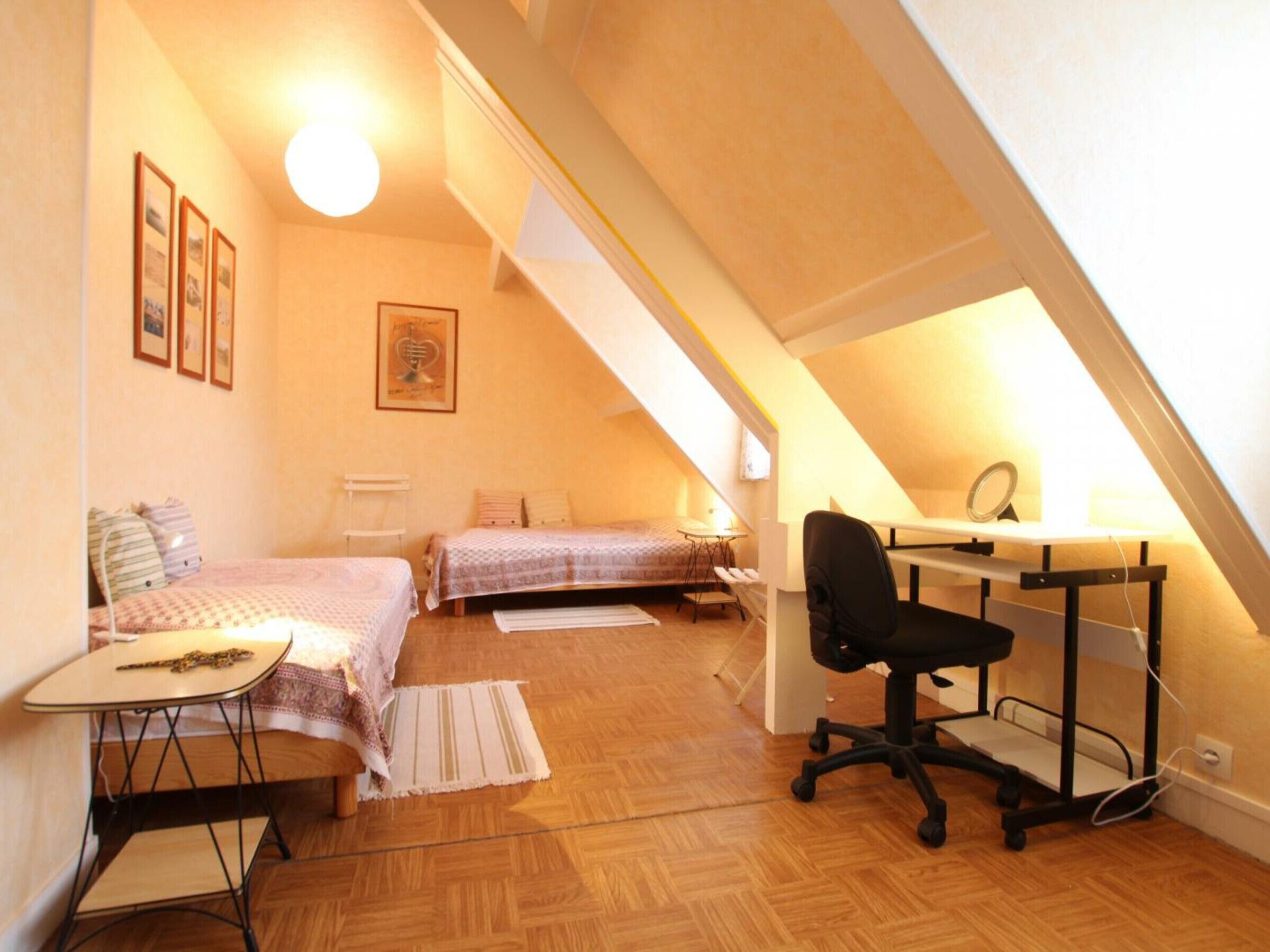 A small, cozy attic bedroom with two beds, a desk with a chair, and a mirror.