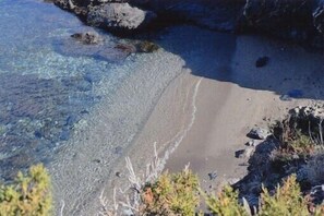 Ein Strand mit klarem Wasser, sandigem Ufer und Felsen.