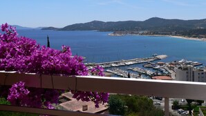 A coastal marina with boats docked, a clear blue sea, and a mountainous backdrop.