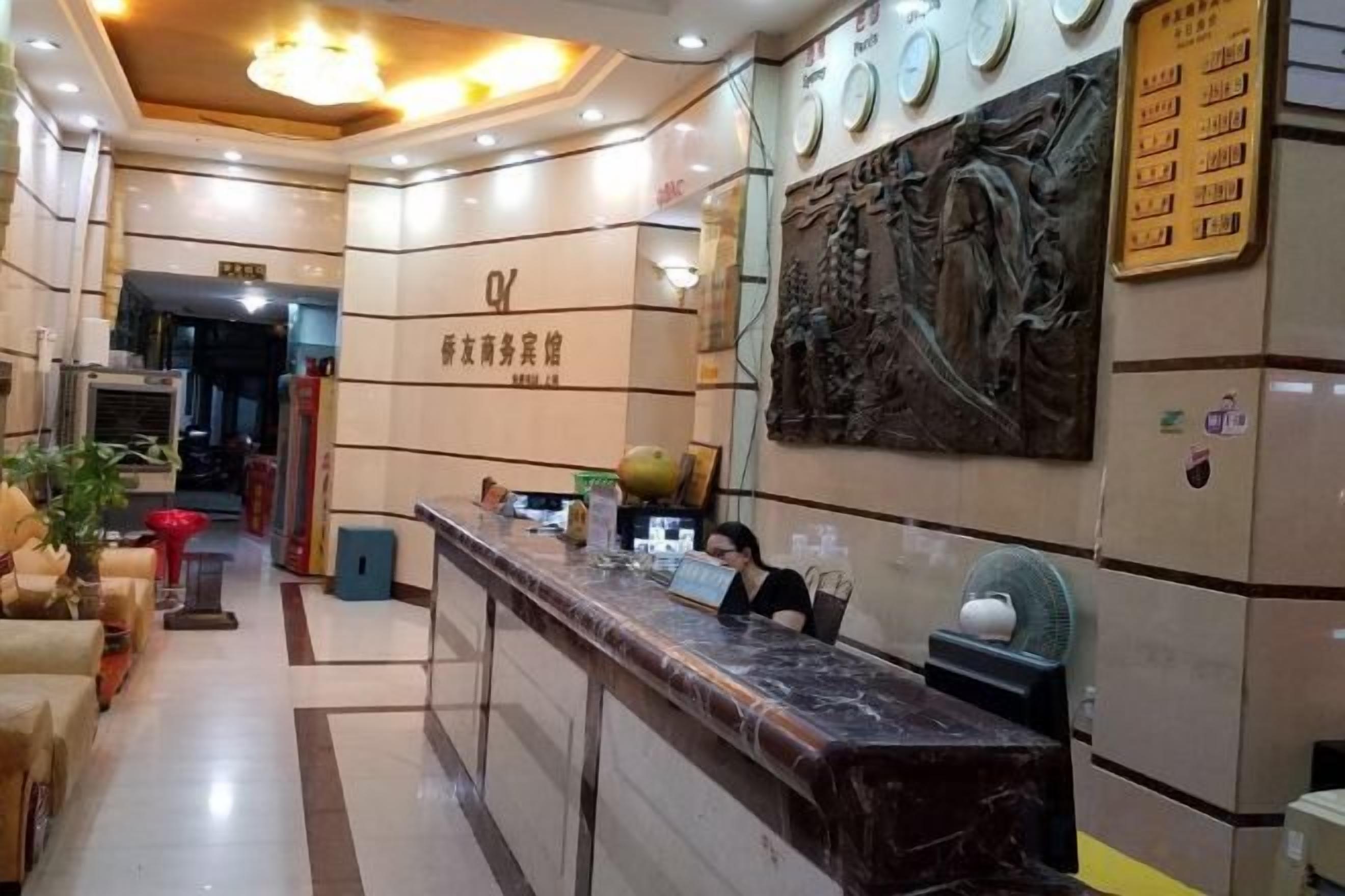 Zona de recepción de un hotel con mostrador de mármol, una recepcionista y un reloj de pared.