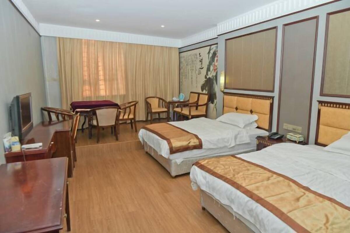 Quarto de hotel com duas camas, uma mesa, uma cadeira, uma mesinha e uma televisão.