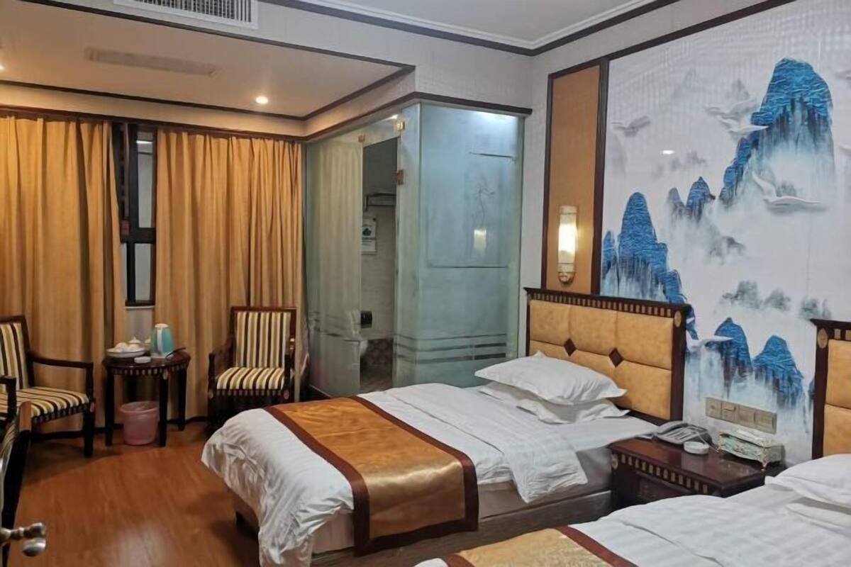 Quarto de hotel com duas camas, uma mesa pequena, uma cadeira, uma mesinha de cabeceira e um quadro na parede.
