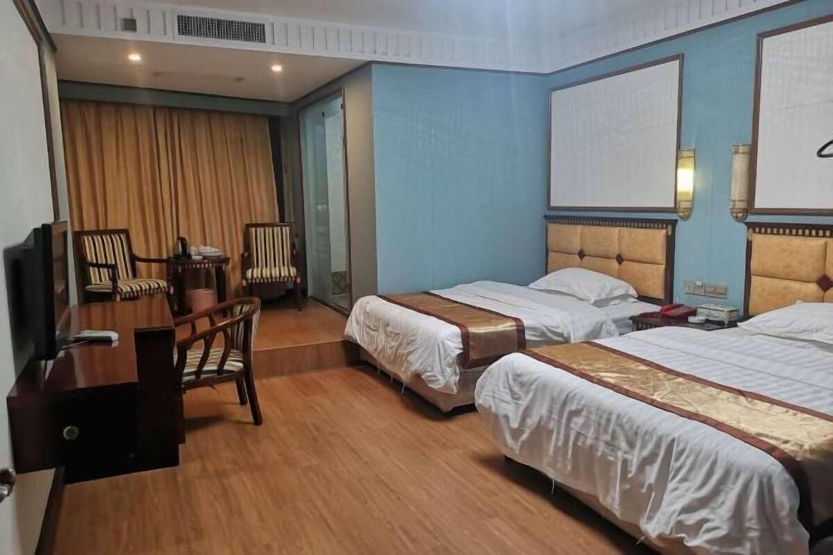 Quarto de hotel com duas camas, uma escrivaninha, cadeiras e uma televisão.