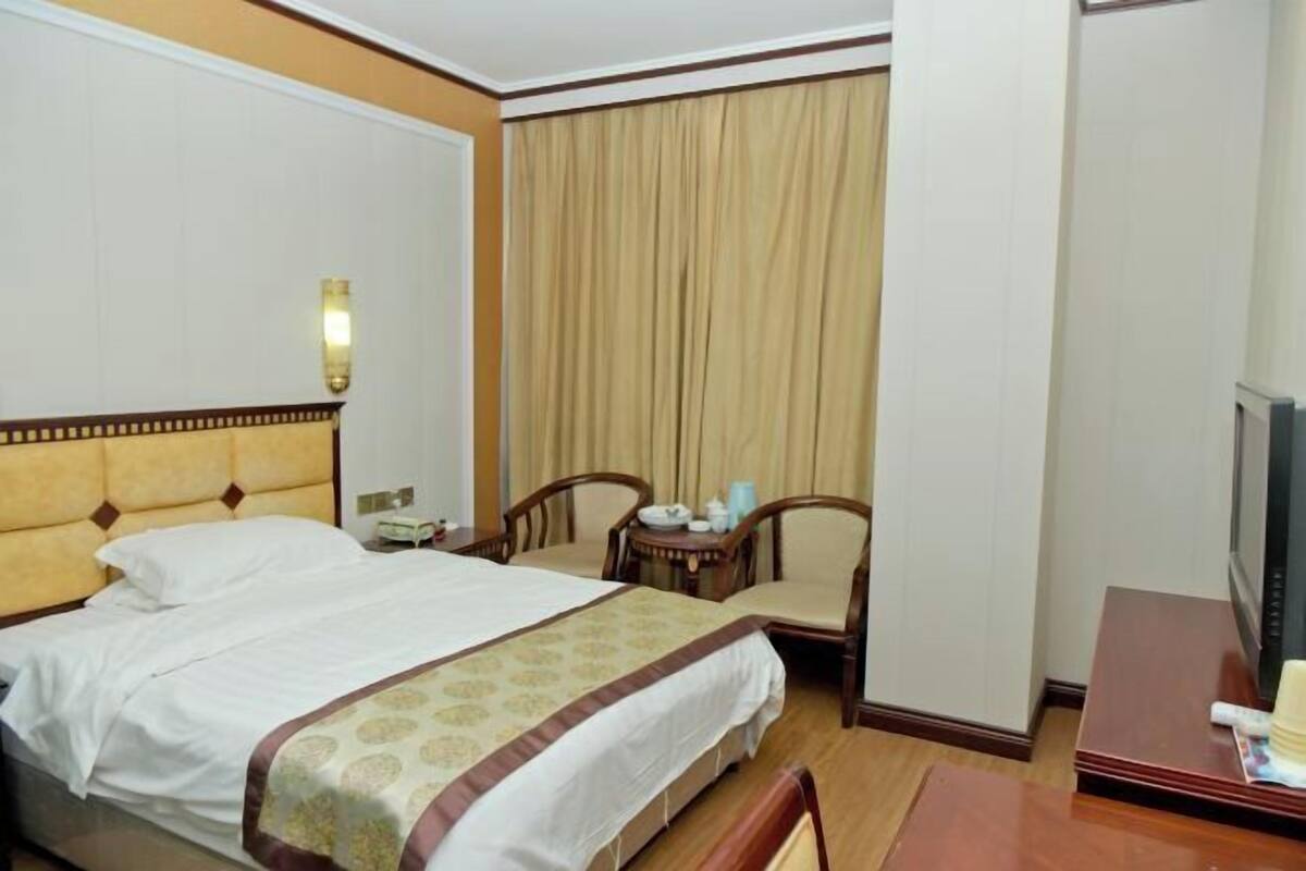 Quarto de hotel com cama, escrivaninha, cadeira, televisão e janela com cortinas.