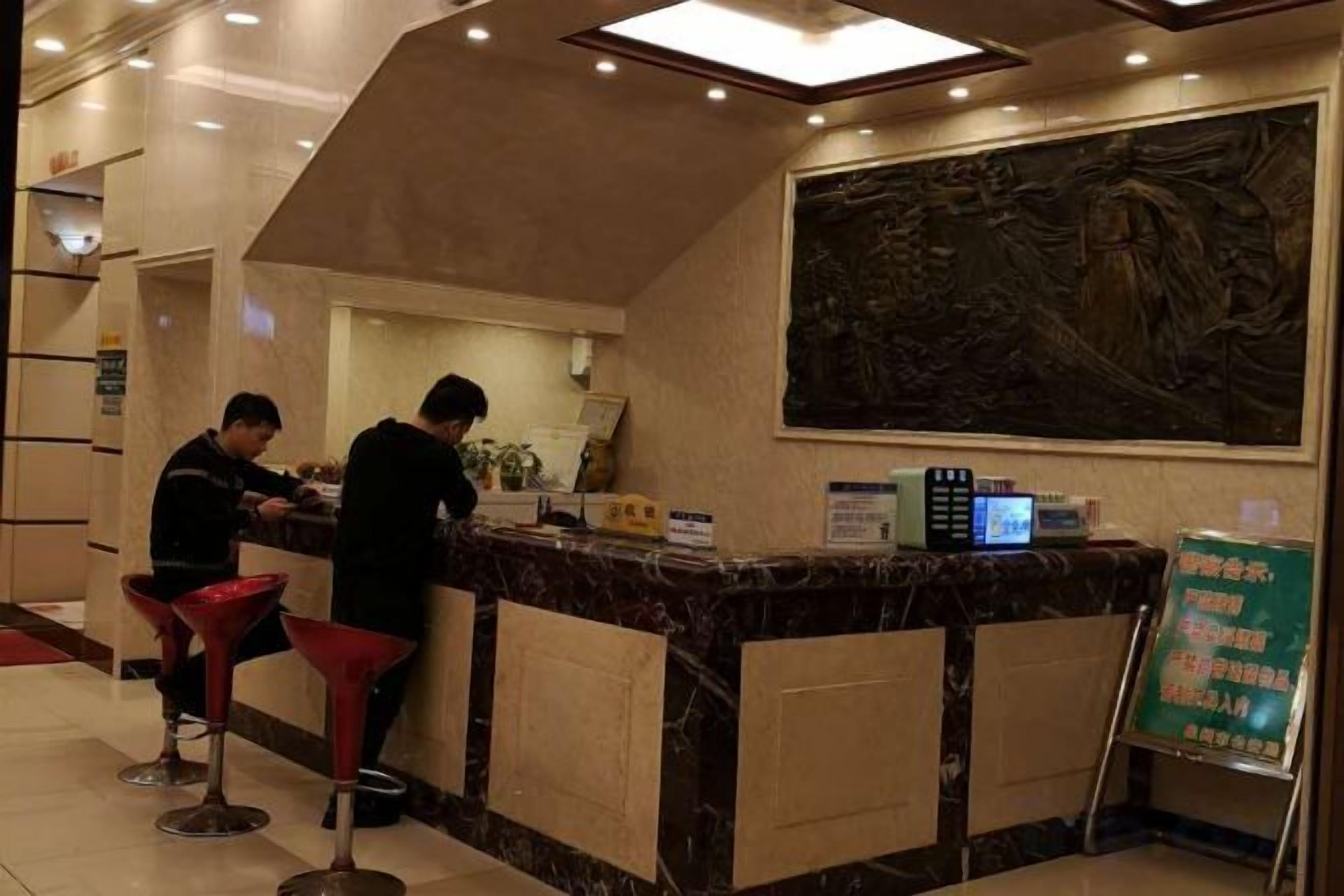 A hotel reception area with a marble counter, red bar stools, and a digital screen.