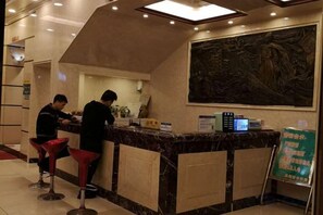 A hotel reception area with a marble counter, red bar stools, and a digital screen. - Quanzhou Yongchun Qiaoyou Business Hotel (Yongchun)
