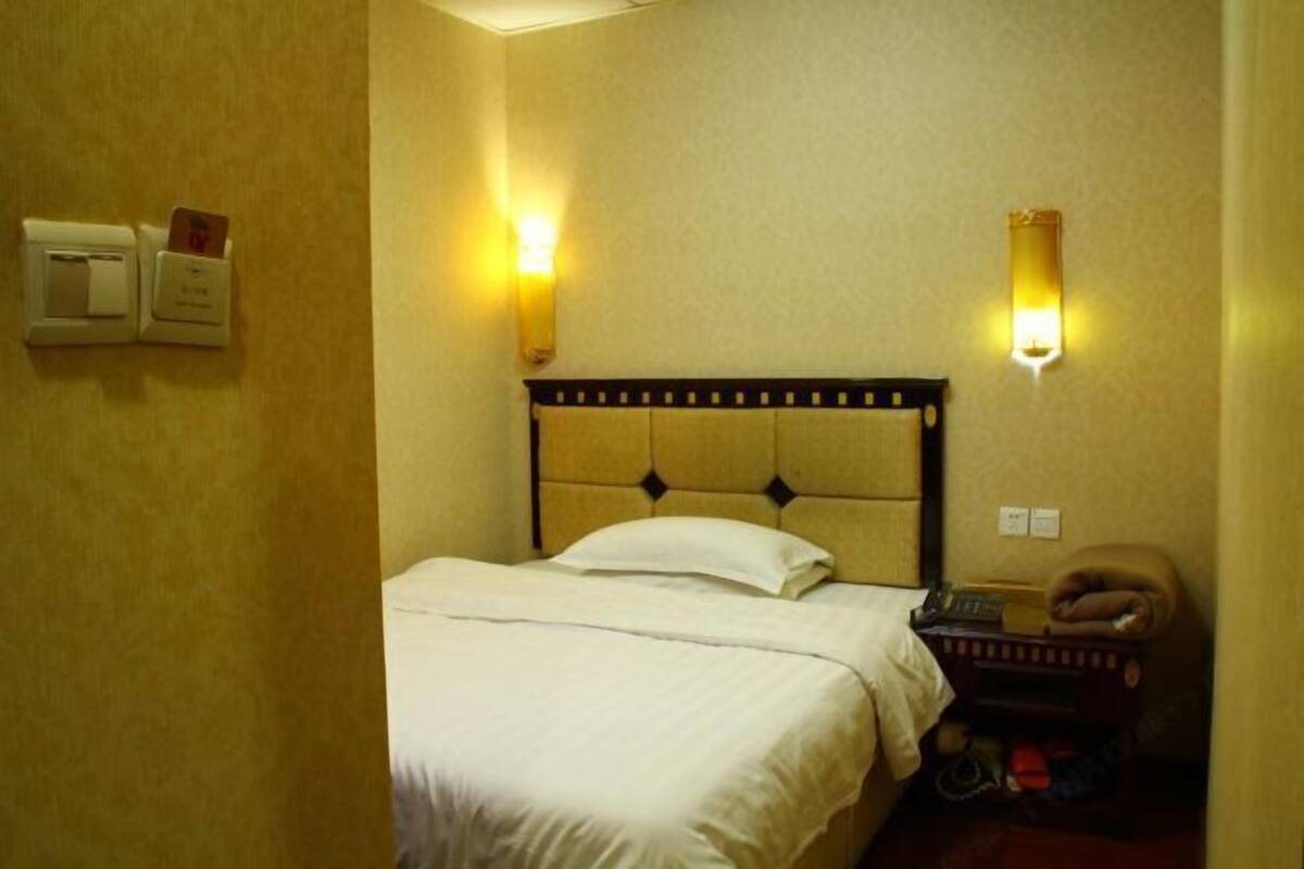 Quarto de hotel com cama, abajures, telefone e um pequeno espaço de estar com um pufe.