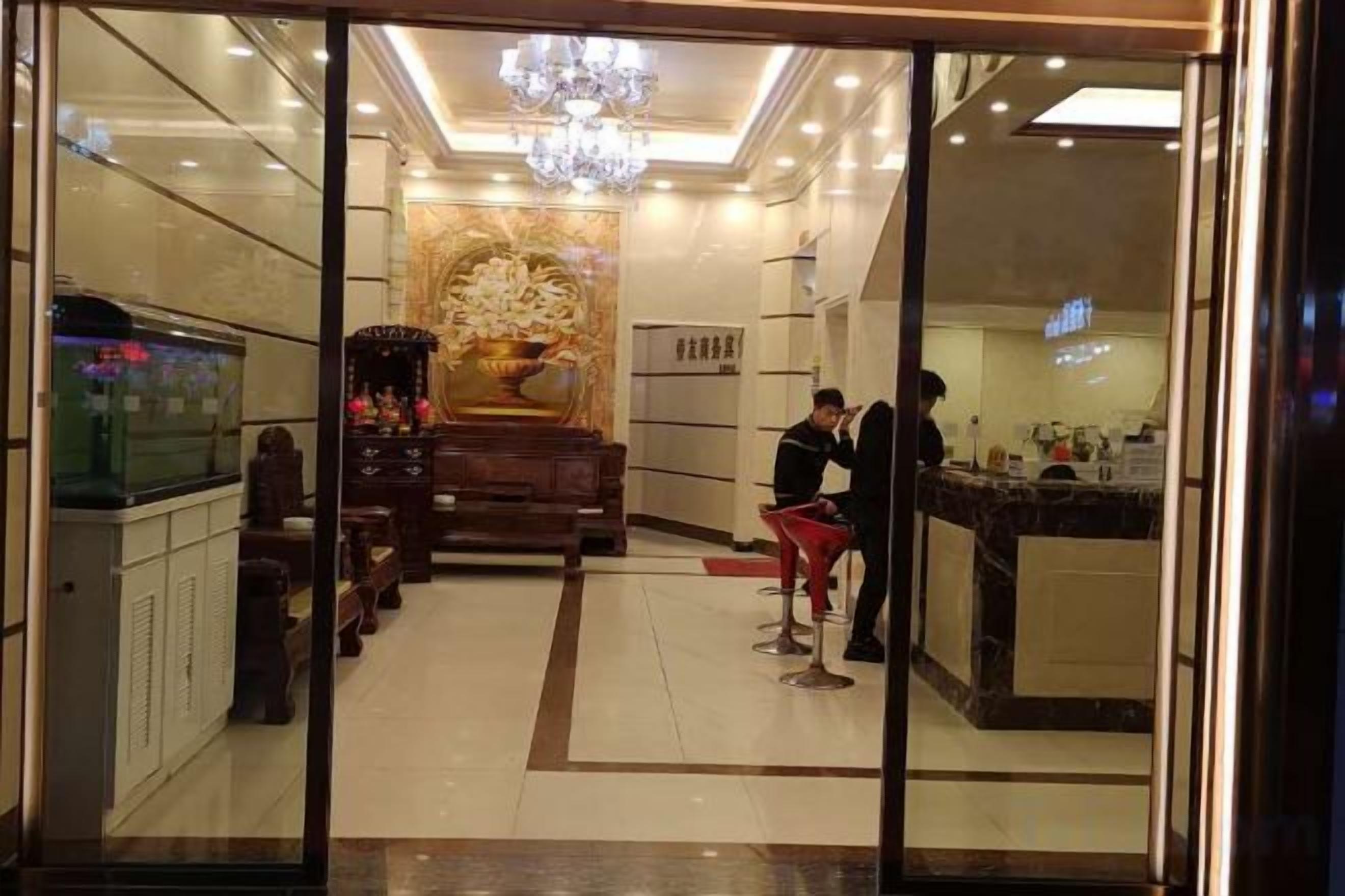 A hotel lobby with a reception desk, a large decorative wall, and a chandelier.