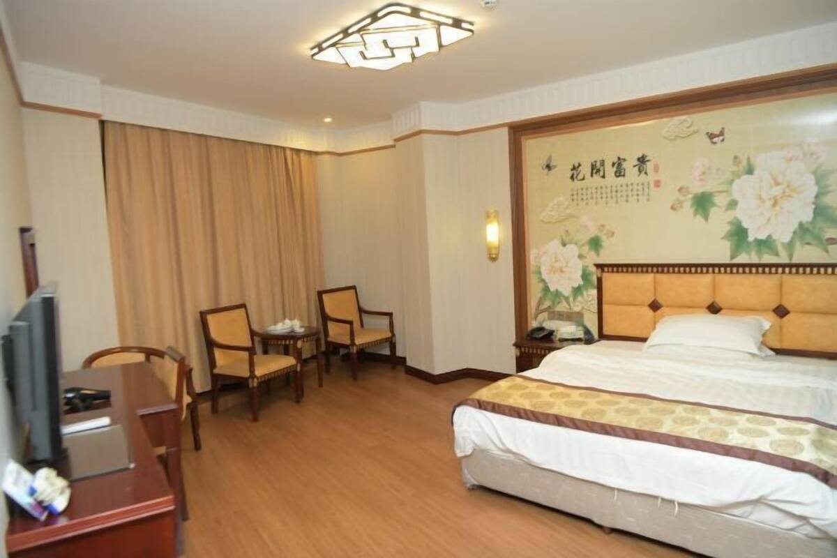 Quarto de hotel com cama, escrivaninha e cadeira, televisão e painel floral na parede.