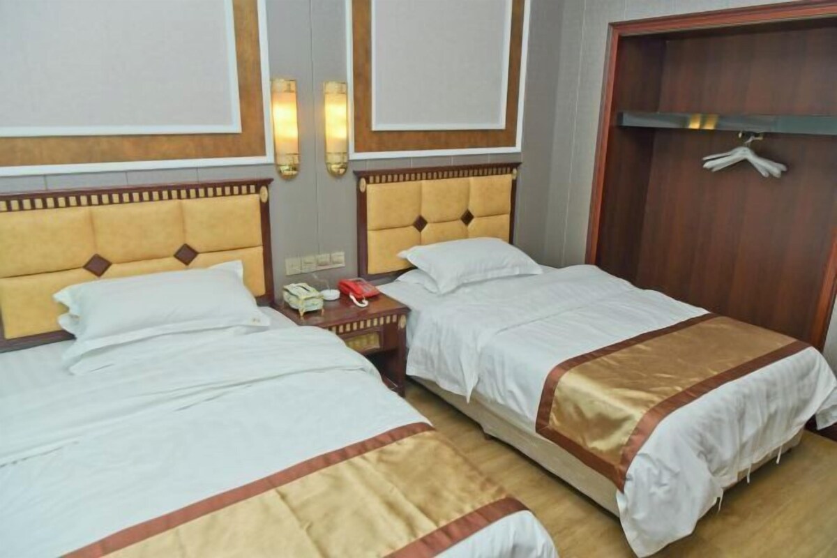A hotel room with two beds, each with a headboard, bedside tables, and a wardrobe.