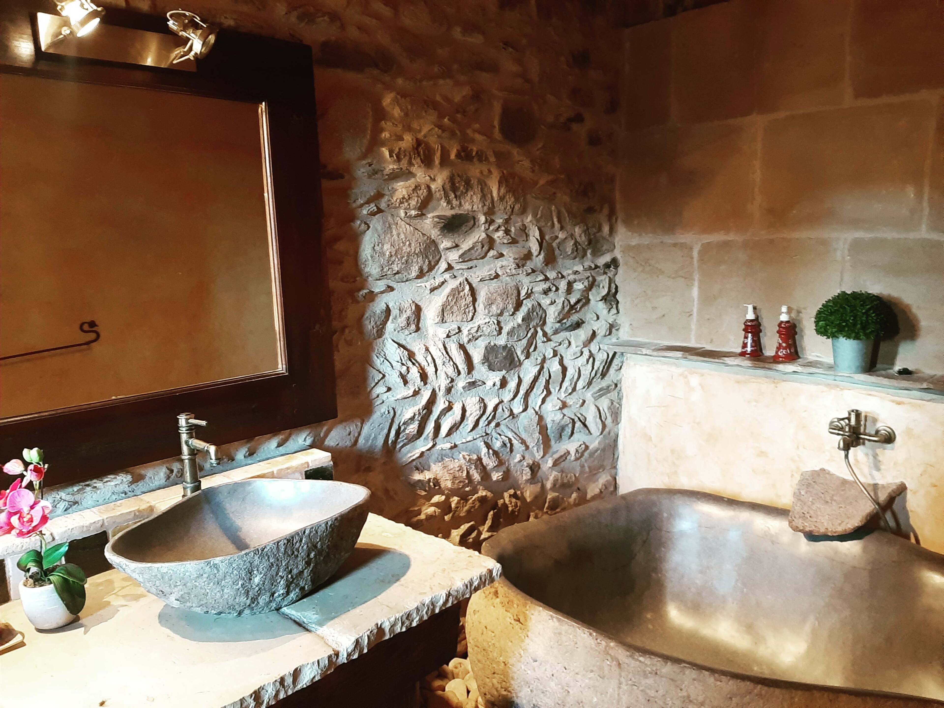 A bathroom with a stone sink, a large bathtub, and a mirror.