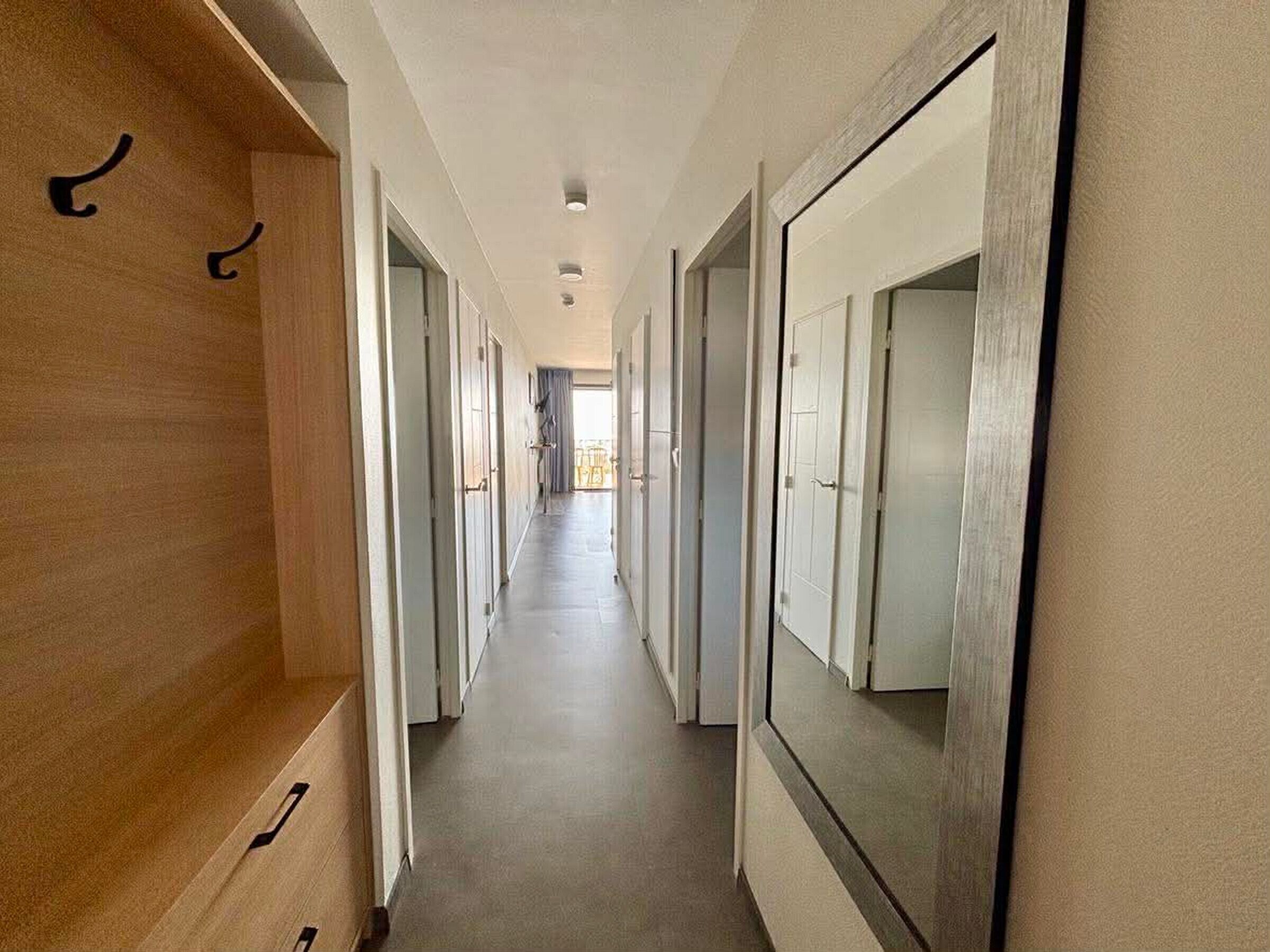 Un pasillo largo y estrecho con taquillas de madera a un lado y puertas espejadas al otro.
