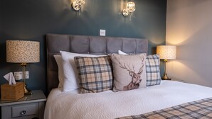 A neatly made bed with a grey headboard, two bedside lamps, and a bedside table with a tissue box. - Sunnyside B and B (Keswick)