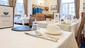 A dining table set with a breakfast menu, a glass, a cup, and cutlery. - Sunnyside B and B (Keswick)