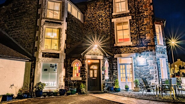 A stone building with multiple windows, a door, and outdoor seating. - Sunnyside B and B (Keswick)