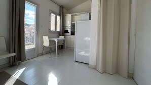 A small, bright kitchen with white cabinets, a refrigerator, and a dining area with a table and chairs.