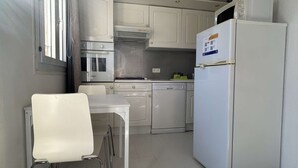 A compact kitchen with white cabinets, a built-in oven, a dishwasher, and a refrigerator.