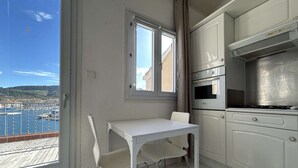 A small kitchen with a dining table and chairs, a window with a view of a harbor, and a stove.