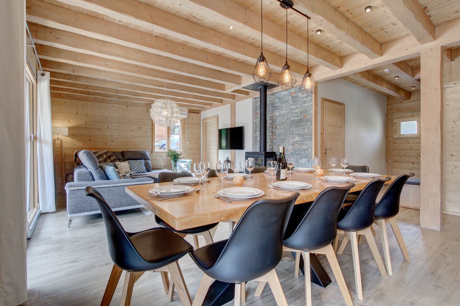 Un comedor moderno con una mesa de madera preparada para seis comensales, sillas negras y una pared de piedra al fondo.
