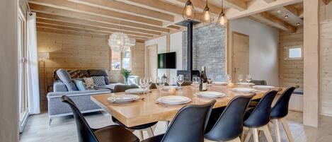 Un comedor moderno con una mesa de madera preparada para seis comensales, sillas negras y una pared de piedra al fondo.