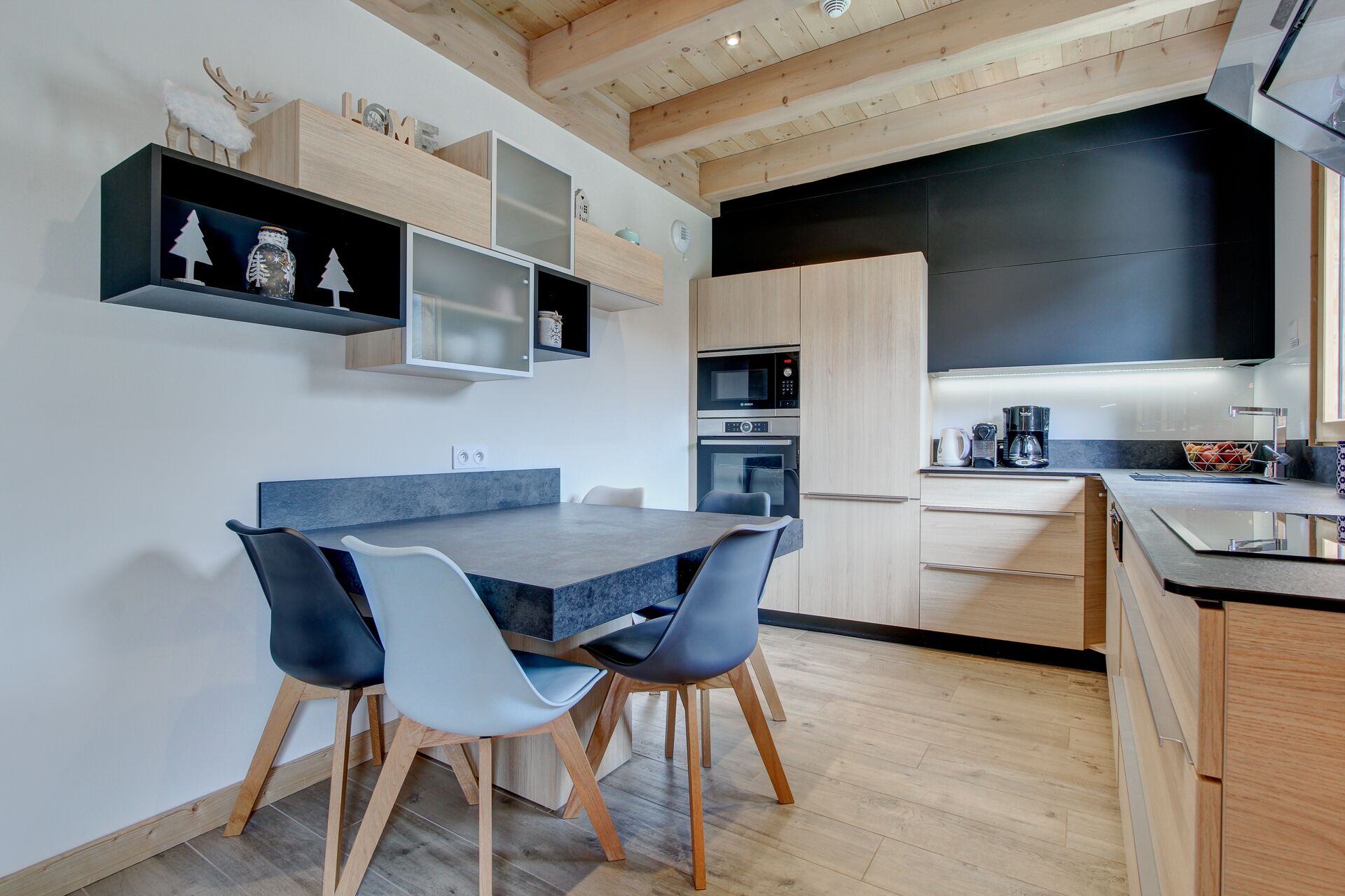 A modern kitchen with a dining area, featuring wooden cabinetry, a built-in oven, and a coffee maker.