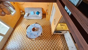 Tunnelmallinen huone, jossa on ruutukuviollinen lattia, tyynyillä varustettu sohva, kuvioitu pöytäliina ja ikkunassa verhot.