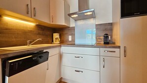 Moderni keittiö, jossa on valkoiset kaapit, sisäänrakennettu astianpesukone, kahvinkeitin ja liesi.