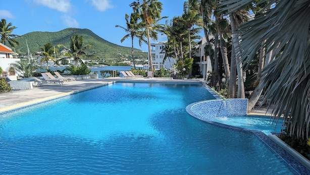 A swimming pool with lounge chairs, palm trees, and a mountainous backdrop.