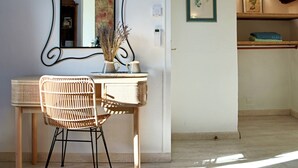 Quarto com escrivaninha, duas cadeiras de vime, espelho e um vaso com flores secas.