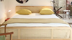 Cama com cabeceira em tear, duas almofadas, abajur e obra de arte na parede.