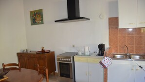 Eine Küche mit Herd, Backofen, Spüle und Schränken. Ein Esstisch mit Stühlen und ein Bild an der Wand sind ebenfalls vorhanden.
