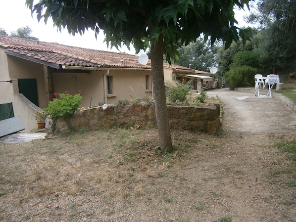 A rustic house with a tiled roof, a stone wall, and a small garden area.