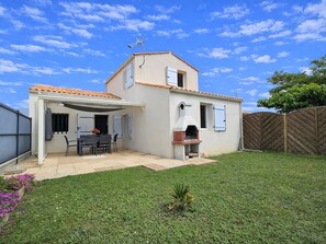 A two-story house with a patio, a barbecue area, and a fenced backyard.