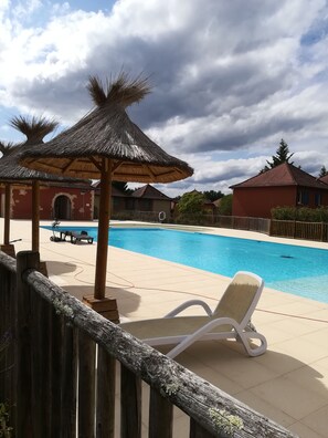 Una piscina con sillas de descanso y una sombrilla de paja, rodeada de vallas de madera y edificios.