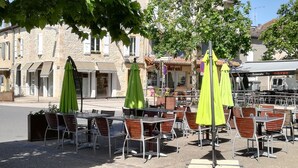 Uteservering med gröna parasoller, byggnader i sten och en skylt med texten ”Hotel de Tourisme”.