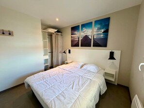 A bedroom with a bed, a nightstand, a lamp, a wardrobe, and a painting on the wall.