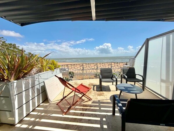 A balcony with a view of the beach, outdoor furniture, and potted plants.