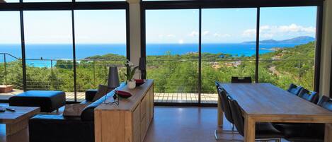 Amplia habitación con grandes ventanales que ofrecen vistas al mar y al follaje.