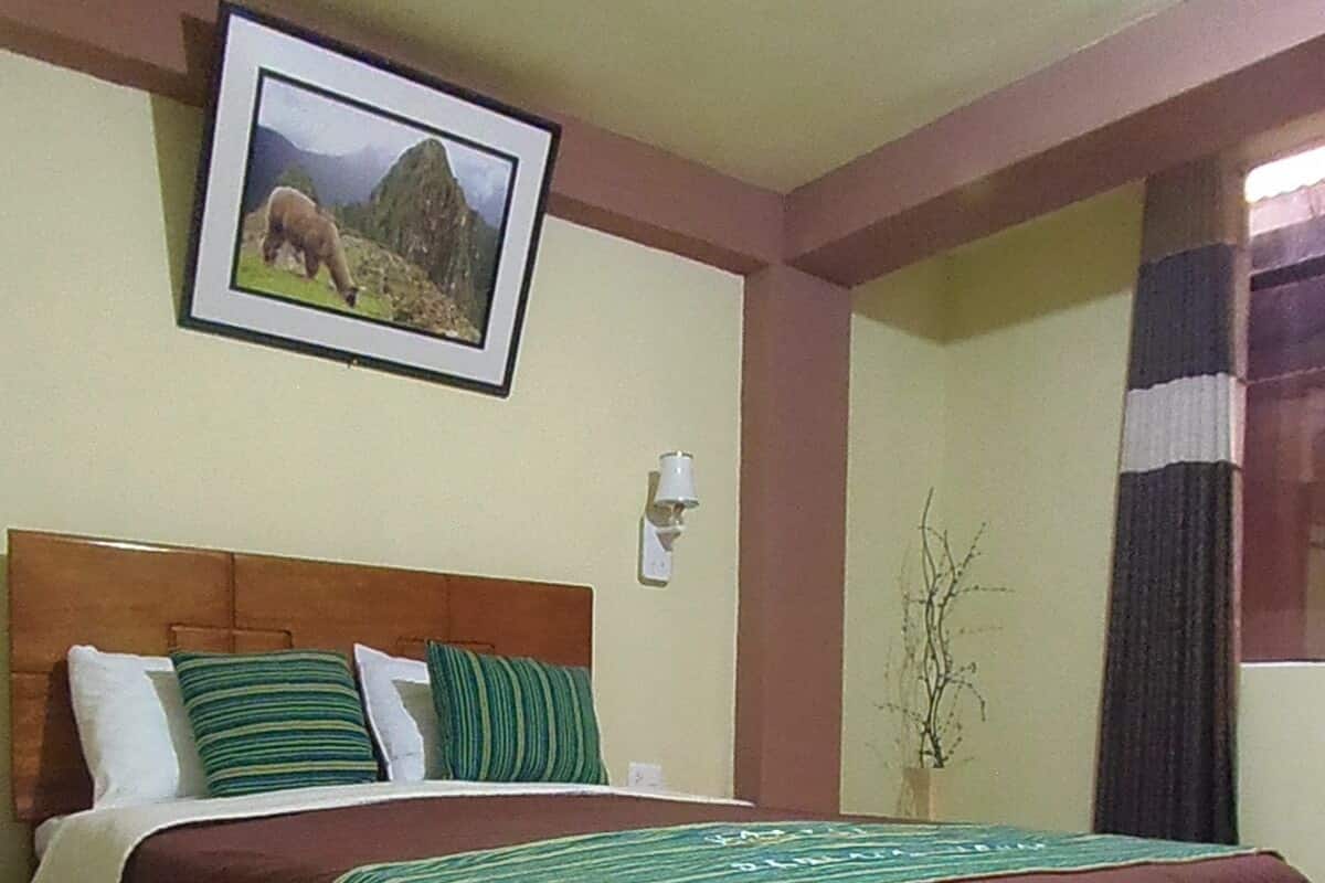 Uma cama com cabeceira marrom, almofadas e manta listradas em verde e branco.