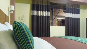 A hotel room with a bed, striped pillow, curtains, and a view of a building outside. - Hostal Pablos House (Machu Picchu)