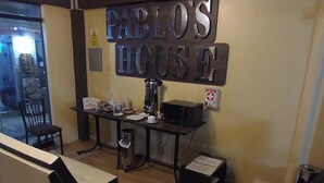 A small, cozy room with a sign reading "Pablo's House". It includes a table with a coffee machine, a chair, and a trash can. - Hostal Pablos House (Machu Picchu)