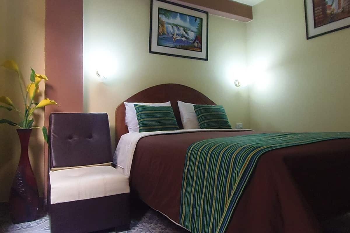 Quarto de hotel com cama, uma cadeira, um vaso com flores e duas luminárias.